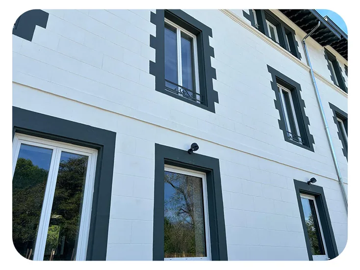 Façade blanche à volets et menuiseries vert foncé, vue en contre-plongée