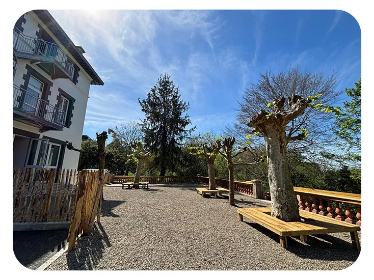 Cour en gravier avec bancs en bois et grand arbre devant le bâtiment