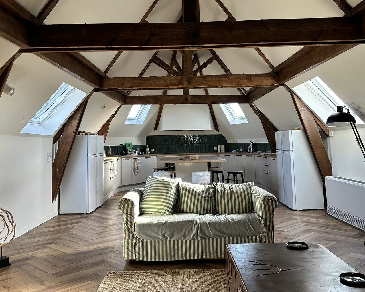 Coin salon des combles vu depuis l'entrée, charpente bois et fenêtres de toit
