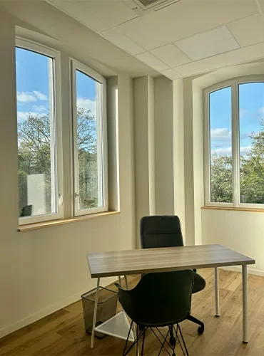 Bureau d'angle meublé d'une table et d'un fauteuil devant trois fenêtres