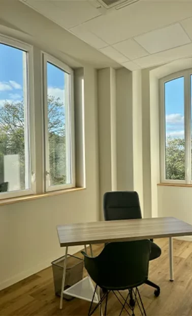 Bureau d'angle meublé d'une table et d'un fauteuil devant trois fenêtres