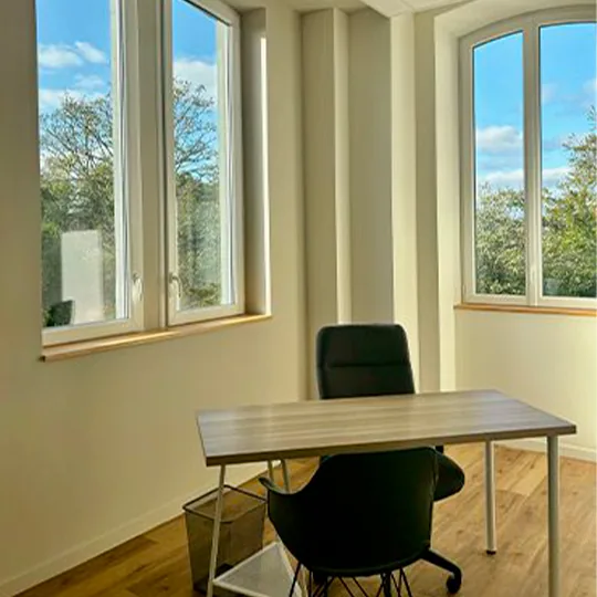 Salle de travail lumineuse, table et chaises installées devant deux fenêtres
