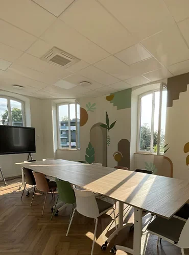 Salle de réunion vue depuis la porte, écran mural et décor végétal peint