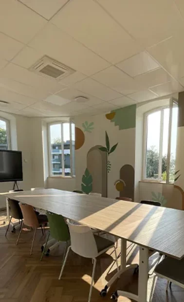 Salle de réunion vue depuis la porte, écran mural et décor végétal peint